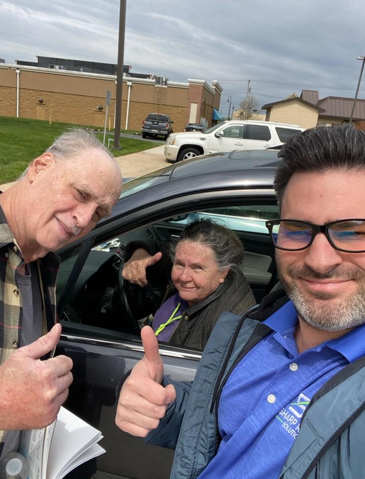 Three men smiling in a car, giving thumbs up